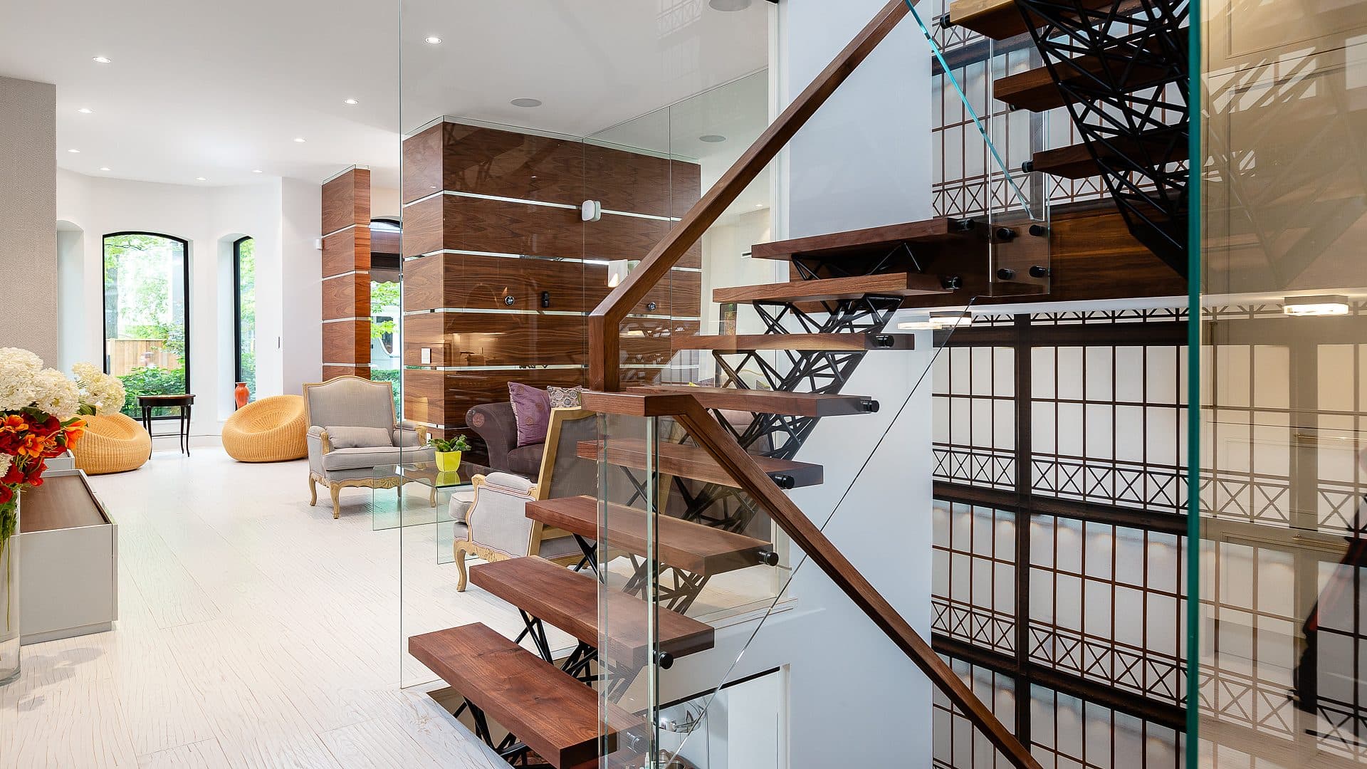 Black steel lattice stair railing with walnut treads and glass balustrade, an antique gilt clock mounted on the decorative wire panel.