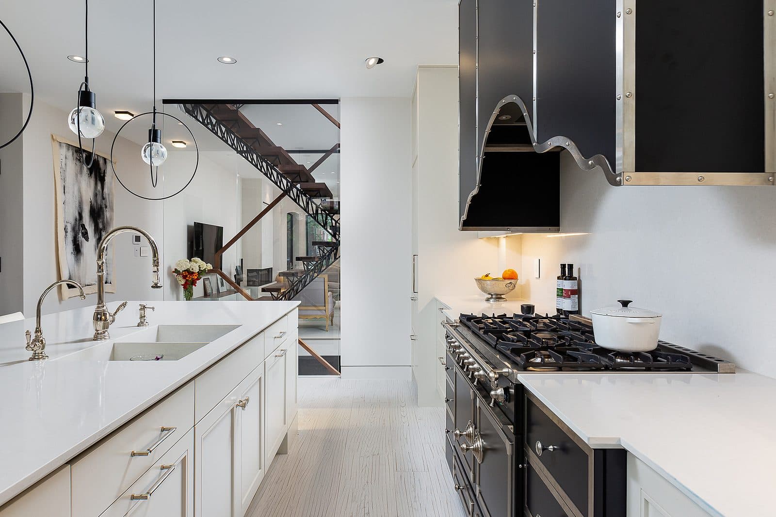 Kitchen counter with marble slab hood, gas range, and view past the island toward a floating steel staircase.
