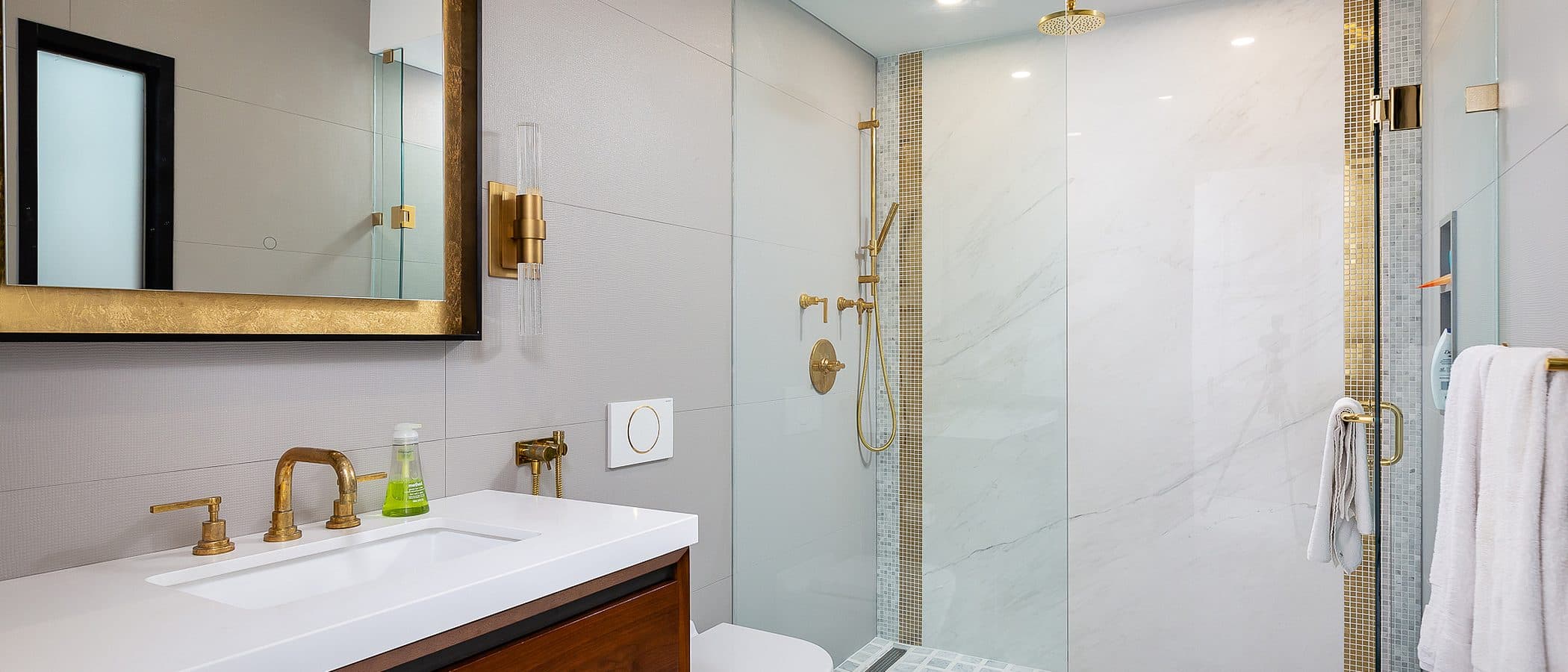 Walk-in glass shower with book matched marble wall, black rain shower head, and matte black fixtures beside a walnut vanity.
