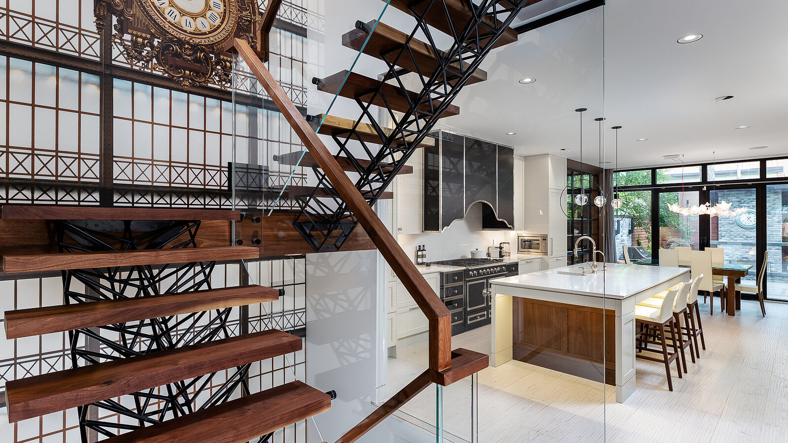 Spiral stair beside a glazed wall with a large station clock and the kitchen beyond