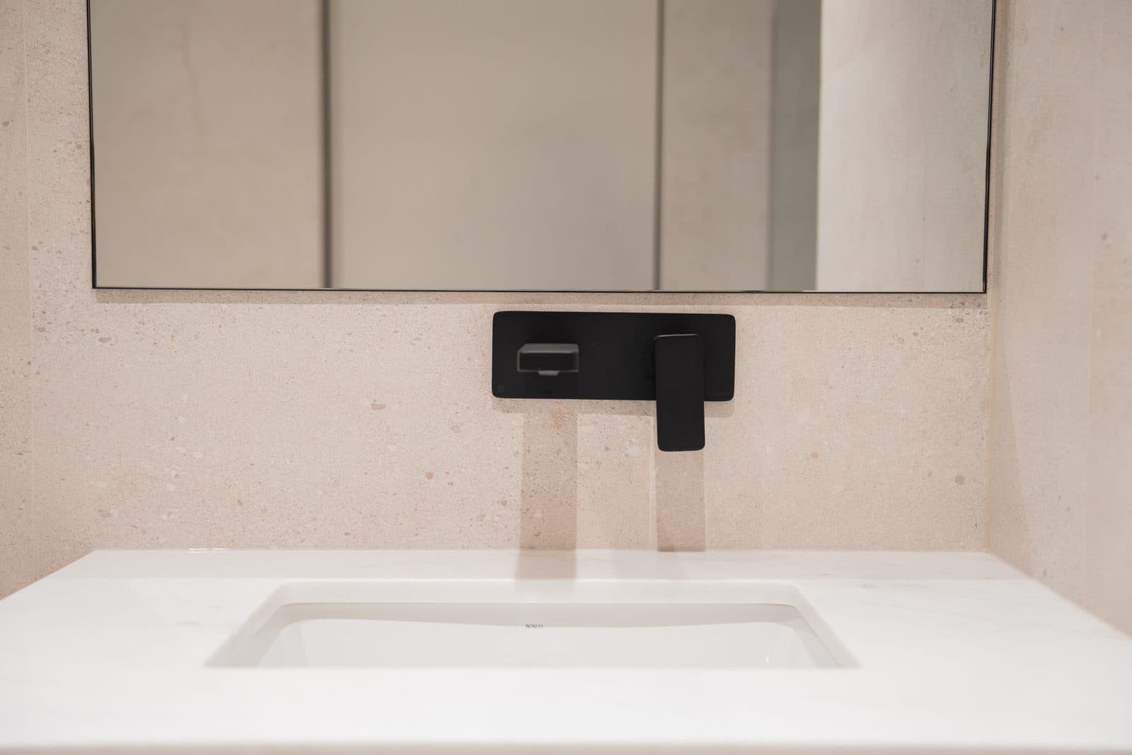 Matte black wall faucet over a white sink on stone tile
