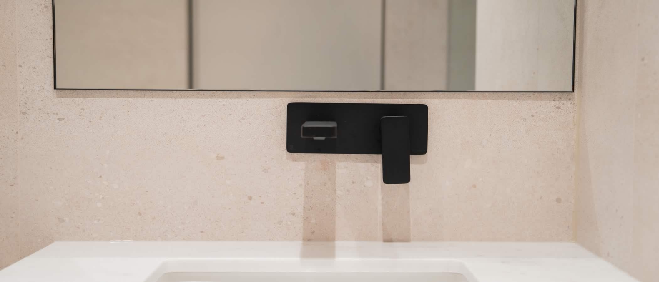 Matte black wall faucet over a white sink on stone tile