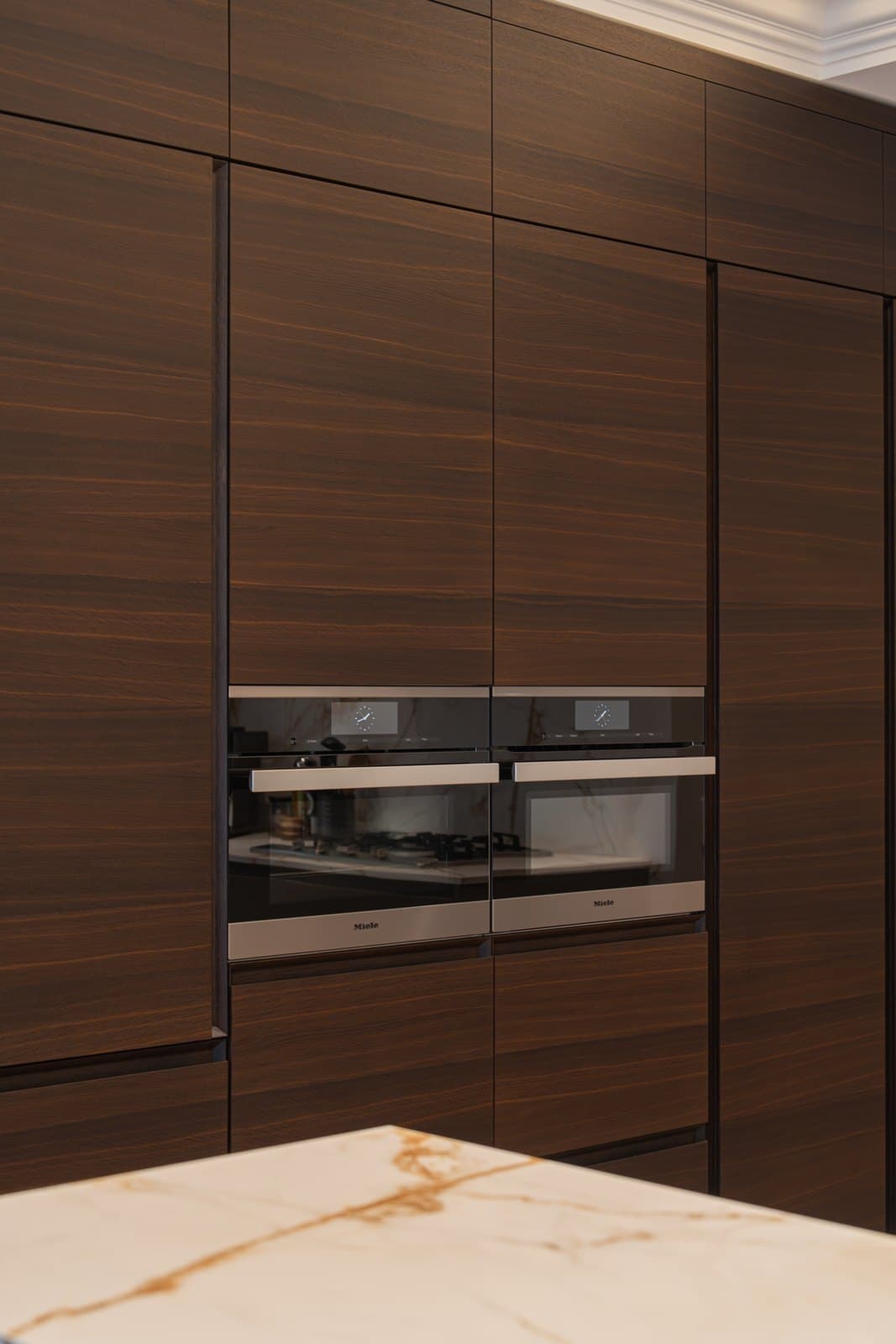 Walnut and marble kitchen with integrated appliances and a book matched stone backsplash