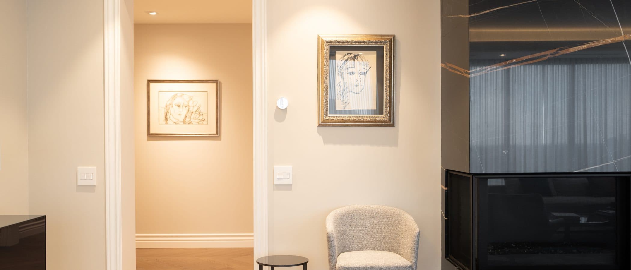 Hallway with sketch portraits in gold frames and a boucle chair