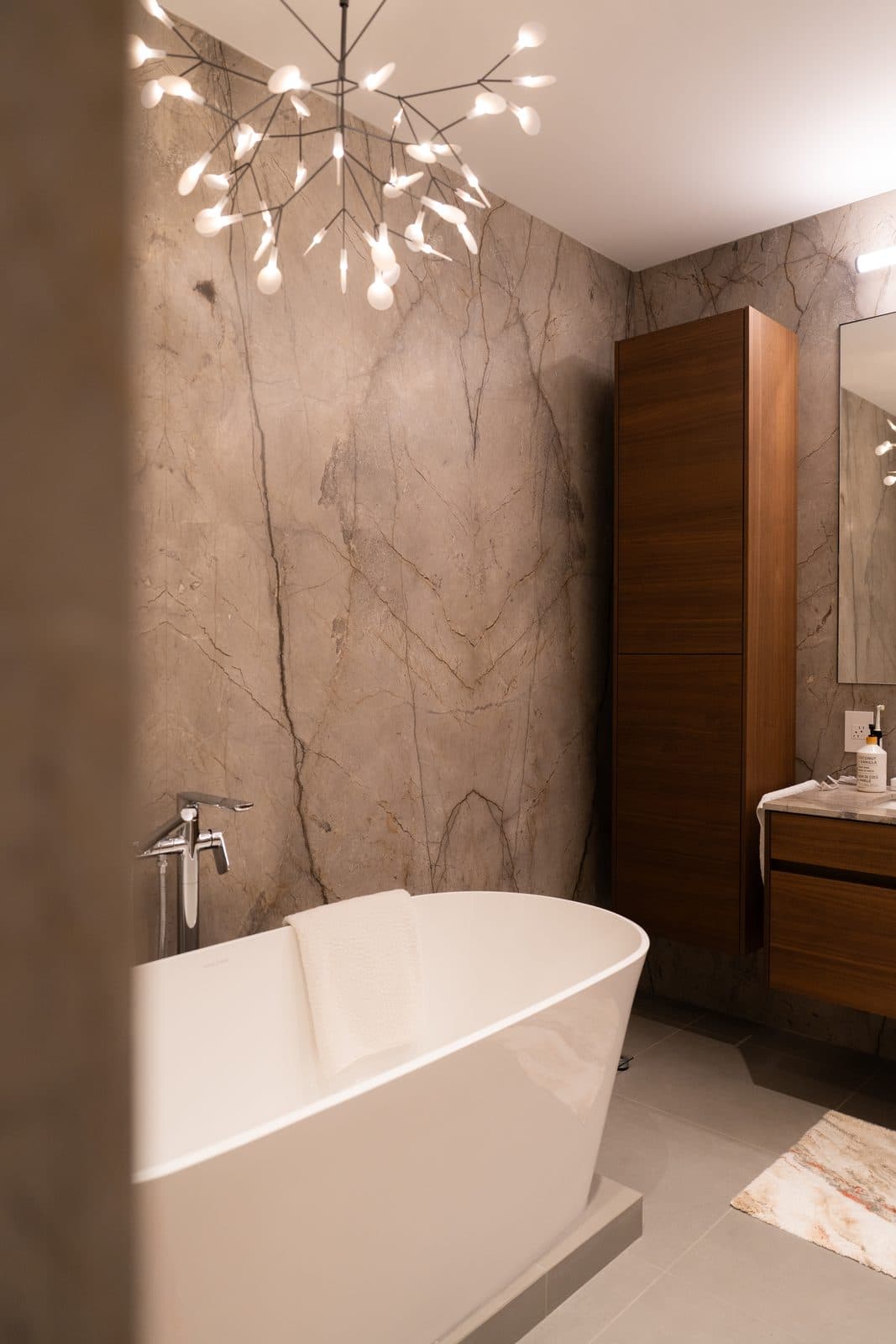Bathroom with a branch form chandelier, freestanding tub and walnut vanity