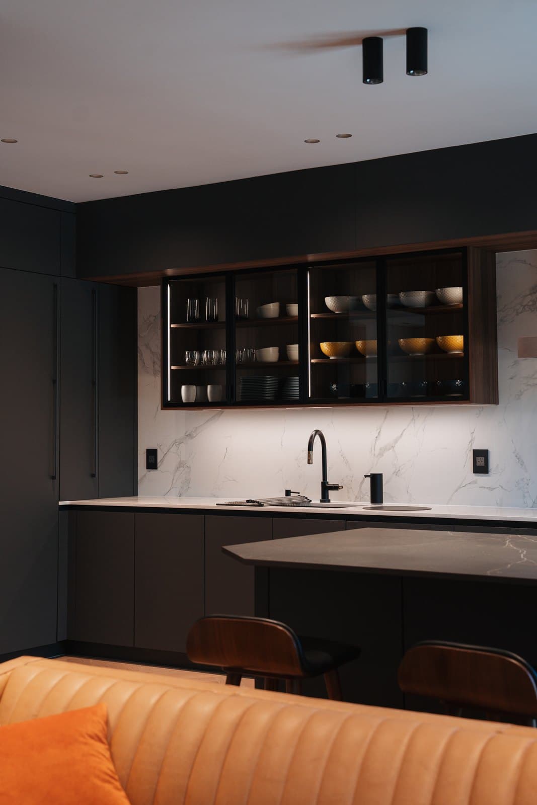 Dark kitchen with a marble backsplash and backlit glass uppers