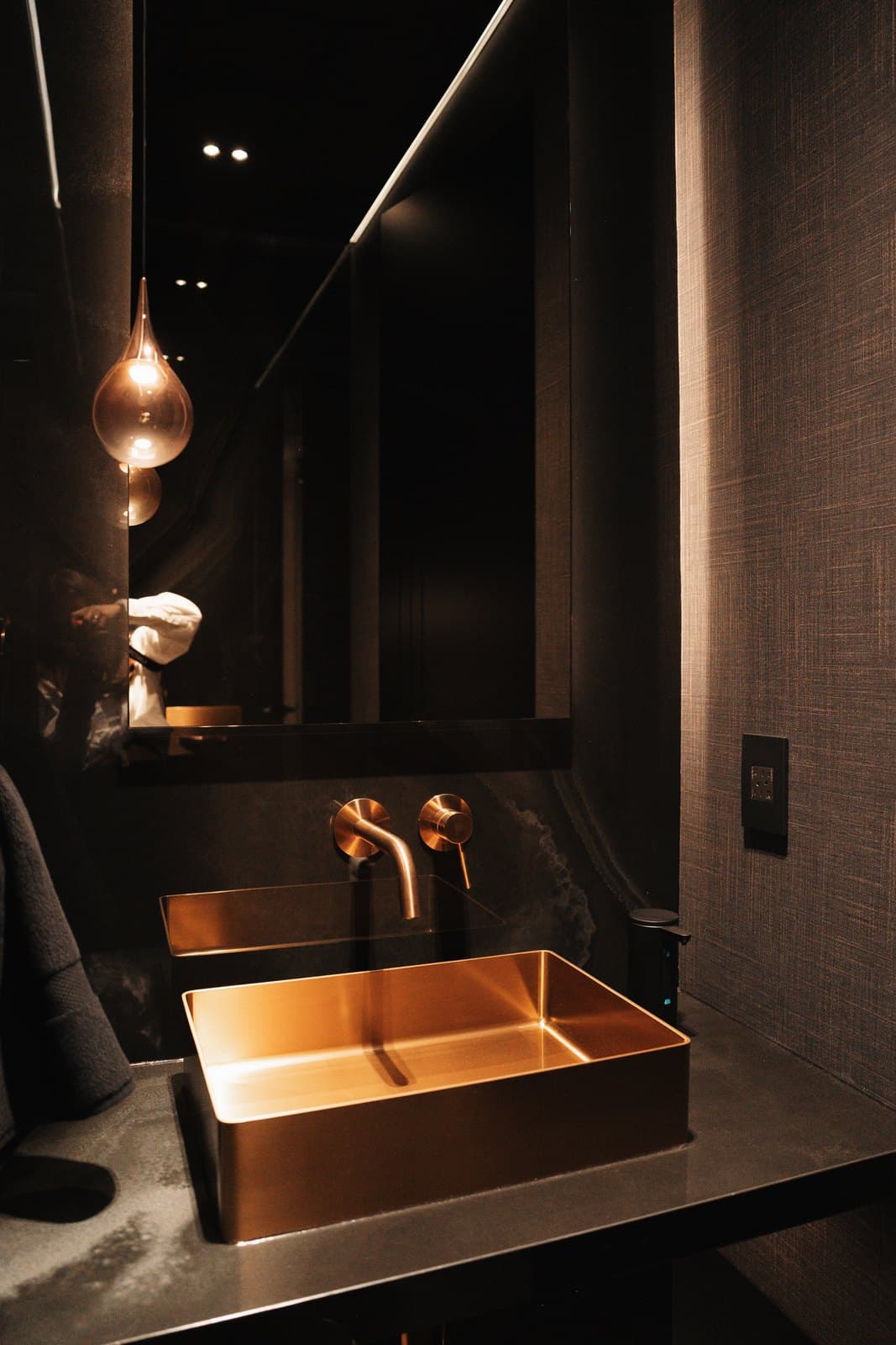 Brass trough sink lit from above in a richly finished powder room