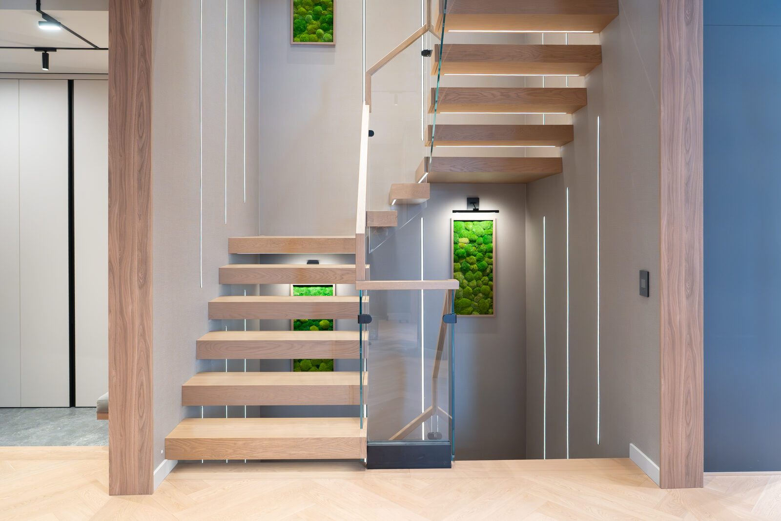 Floating oak stair with backlit moss panels and concealed lighting at the entry